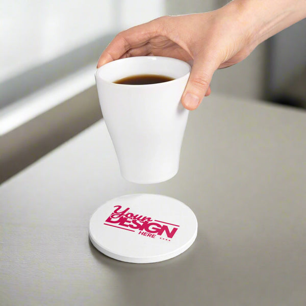 White coaster with 'Your Design Here' text and a hand holding a white cup with coffee.