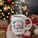 White mug with penguin design held in front of a festive background with lights and presents.
