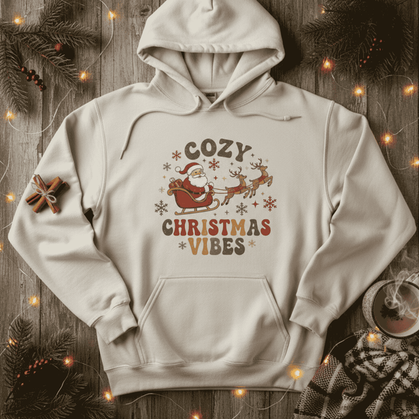 White hoodie with 'Cozy Christmas Vibes' text and Santa Claus design on a wooden background with festive decorations.