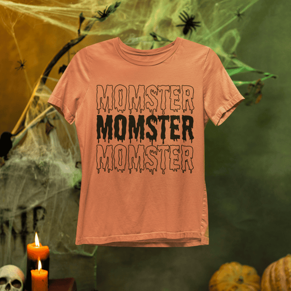 Orange t-shirt with 'MONSTER' text on a Halloween-themed background with pumpkins and candles.